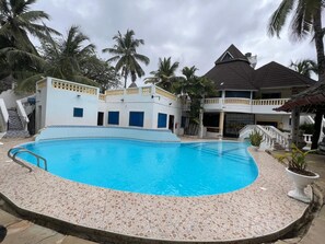 A swimming pool with a tiled deck, surrounded by buildings with balconies and palm trees.
