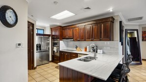 A modern kitchen with wooden cabinets, stainless steel appliances, a marble island, and a built-in sink. - Reserva Conchal Escape With Golf Course Views (Cabo Velas)