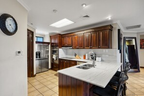 A modern kitchen with wooden cabinets, stainless steel appliances, a marble island, and a built-in sink. - Reserva Conchal Escape With Golf Course Views (Cabo Velas)