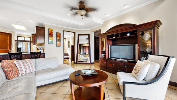 A living room with a sofa, armchair, coffee table, TV, and wooden entertainment center. - Reserva Conchal Escape With Golf Course Views (Cabo Velas)