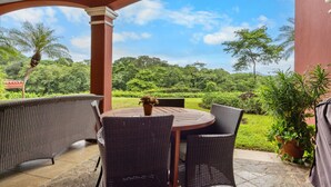 A covered patio with wicker furniture and a view of a lush garden. - Reserva Conchal Escape With Golf Course Views (Cabo Velas)