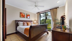 A bedroom with a bed, a desk, a ceiling fan, and a view of the outdoors. - Reserva Conchal Escape With Golf Course Views (Cabo Velas)