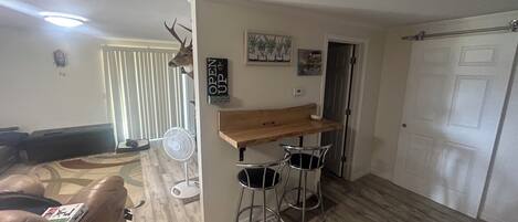 Een woonkamer met een bank, een houten tafel met twee stoelen, een plafondventilator en een decoratie van een hertenkop.
