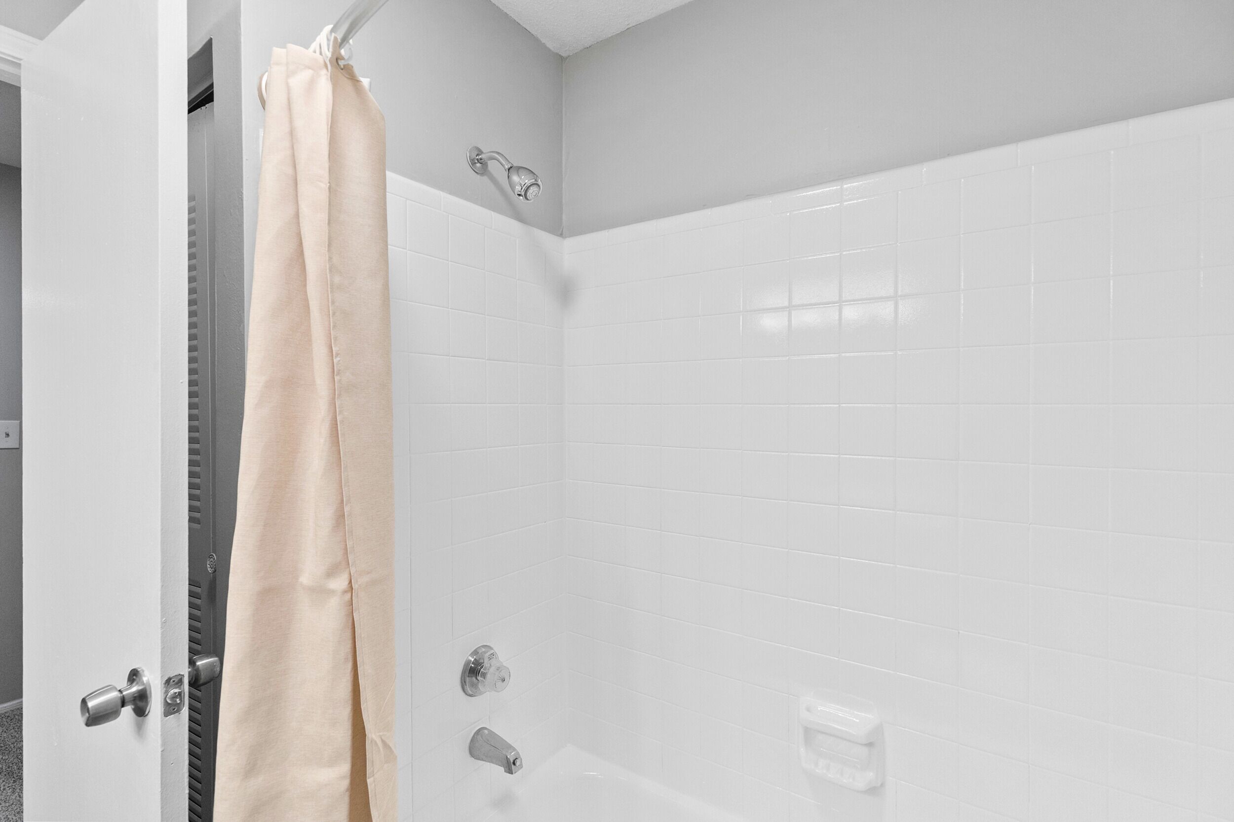 Een badkamer met witte betegelde wanden, een douchegordijn, een bad en een toilet.