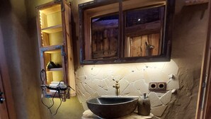 A rustic bathroom with a stone sink, wooden shelves, and a window with a view.