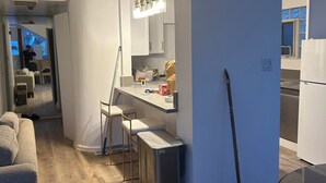 Una cocina moderna con armarios blancos, un bote de basura de acero inoxidable, una escoba y un taburete de bar.