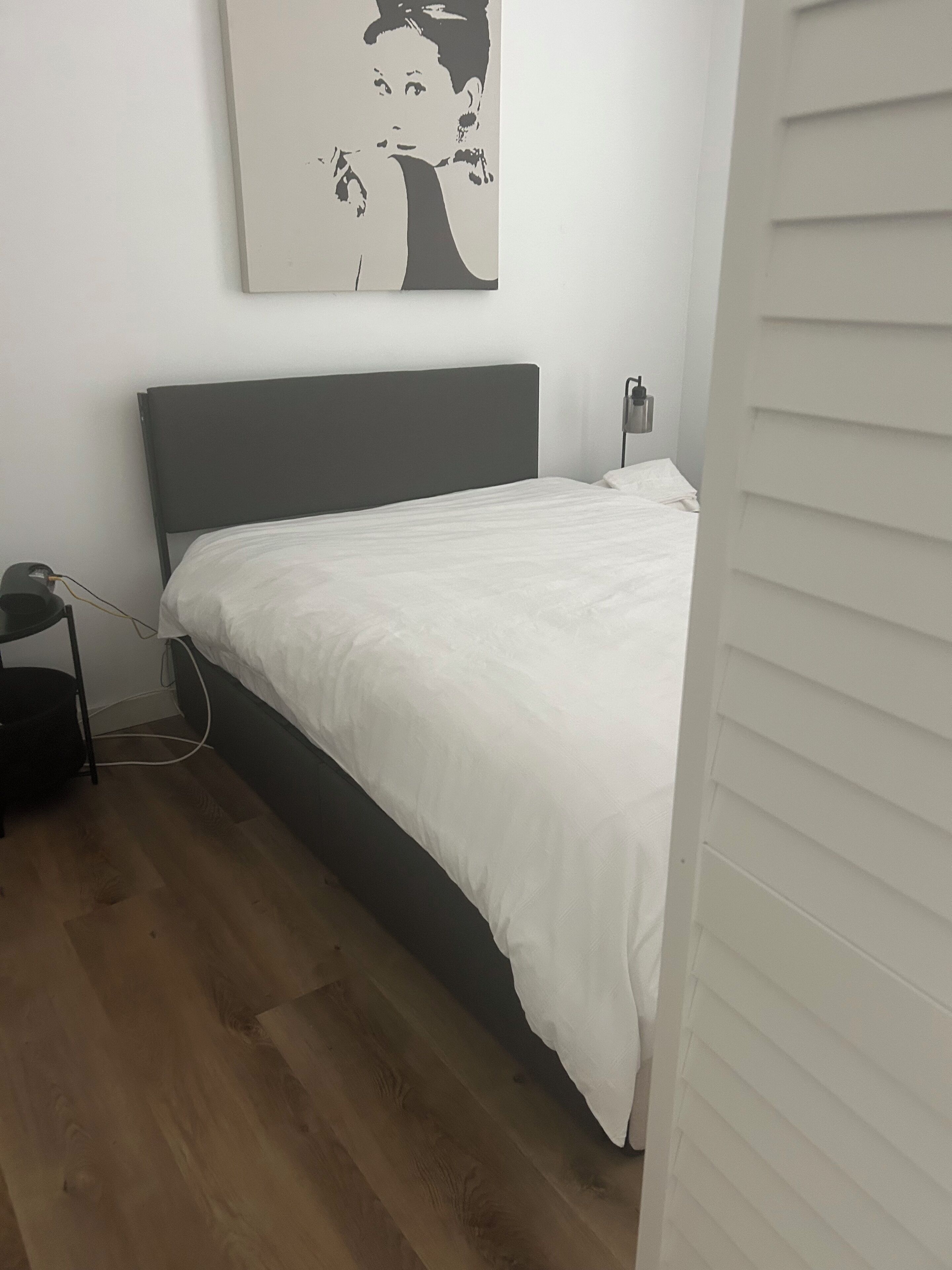 A bedroom with a bed, a bedside table, a lamp, and a wall-mounted artwork.