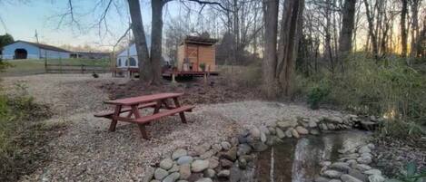 A gravel area with a wooden picnic table and a small stream with a stone border.