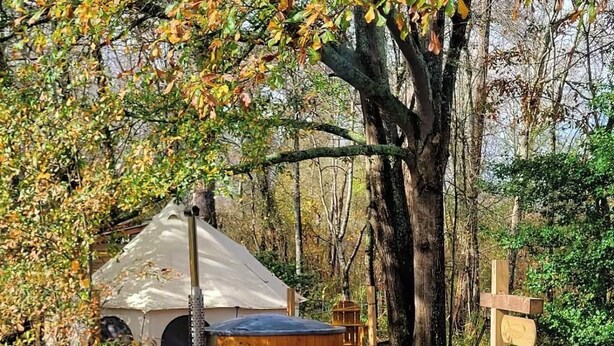 A rustic outdoor setting with a large tent, a wooden hot tub, and a wooden signpost. - Romantic night in nature. Yurt in Piedmont with AC/Heat (Piedmont)