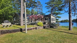 En hytte ved søen med en terrasse, en vindmølle og en båd lagt til ved vandet.