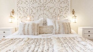 Une chambre à coucher avec une tête de lit décorée, une couvre-lit à motifs et deux lampes de chevet.