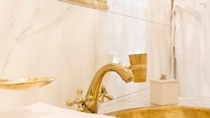 Une salle de bain avec un lavabo doré, un robinet doré, une serviette blanche et un miroir encadré d’or.