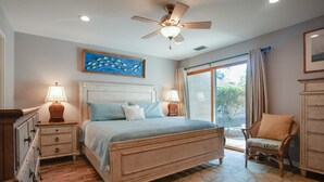 A bedroom with a bed, two bedside tables with lamps, a ceiling fan, a window with curtains, and a chair. - Relax & Unwind|2BR Sea Pines Getaway (Hilton Head Island)