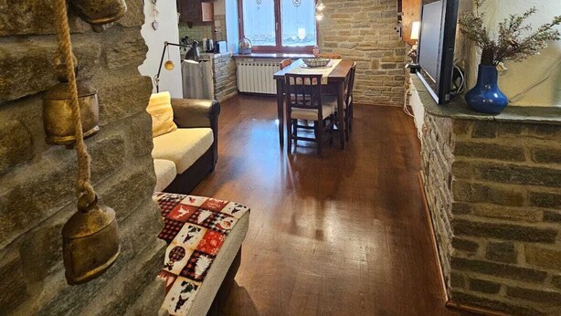 Ein rustikales Interieur mit Steinwänden, Holzbalken, einem Kamin, einem Essbereich und einer Küche.
