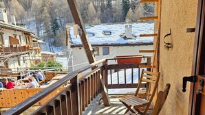 Ein Balkon mit Steinböden, Holzstühlen und Blick auf eine verschneite Landschaft.