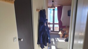En hall med en dörr, en klädhängare med en jacka, en takfläkt och ett fönster med gardiner.