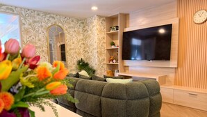 Una sala moderna con un sofá modular, un televisor de pantalla plana en la pared, un espejo decorativo y un mueble de madera.