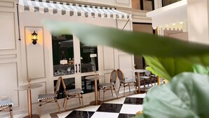 Una cafetería con suelo a cuadros, toldo a rayas y sillas de madera.