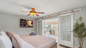 Une chambre à coucher avec un lit, un ventilateur de plafond, une porte-fenêtre coulissante et une plante en pot.
