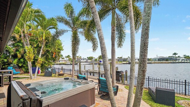 A hot tub, outdoor seating, palm trees, and a waterfront view. - Aruba Breeze Retreat | Hot Tub & Pool Table (Fort Myers)