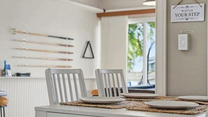 A dining area with a white table set for four, two white chairs, and a wall-mounted sign. - Aruba Breeze Retreat | Hot Tub & Pool Table (Fort Myers)
