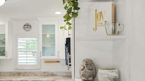 A kitchen with white cabinets, a clock, and a shelf with decorative items. - Aruba Breeze Retreat | Hot Tub & Pool Table (Fort Myers)