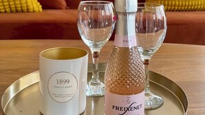 Ein Tablett mit einer Flasche Freixenet Sekt, einer Kerze mit der Aufschrift '1899' und zwei Weingläsern auf einem Holztisch.