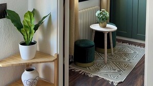 Ein Korridor mit Holzboden, einer grünen Tür, einem kleinen runden Tisch mit einer Pflanze und einem weißen Regal mit einem Topfpflanzen und einer Vase.