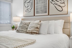 Ein Schlafzimmer mit einem Bett, Kissen, einem Nachttisch mit Lampe und Wandbildern.