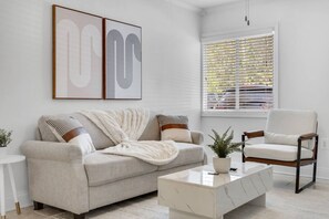Ein Wohnzimmer mit Sofa, Sessel, Couchtisch und einem Kunstwerk an der Wand.
