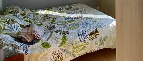 A room with a bed, a small wooden dresser, a wall-mounted picture, and a ceiling light fixture.