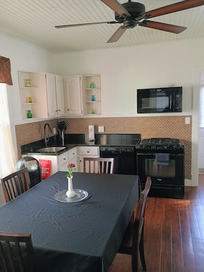 A kitchen with a microwave, oven, and a ceiling fan. There is a dining table with chairs and a vase of flowers.