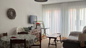 A living room with a dining table, chairs, a sofa, a TV, and a ceiling light fixture. - Apartment in Empuriabrava 150 meters from the sea, in a residence with 3 swimming pools (Empuriabrava)