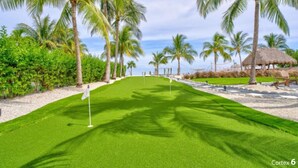 A golf course with a flagstick, palm trees, and a thatched-roof structure. - Paradise Point -Pet friendly 
Oceanfront Luxury with Pool/ Dock/outdoor kitchen. (Marathon)