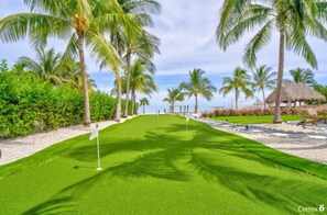 Ein Golfplatz mit einer Fahne, Palmen und einem Gebäude mit einem Reetdach.