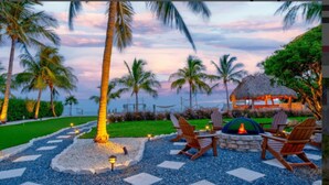 An outdoor seating area with a fire pit, lounge chairs, and a thatched-roof structure. - Paradise Point -Pet friendly 
Oceanfront Luxury with Pool/ Dock/outdoor kitchen. (Marathon)