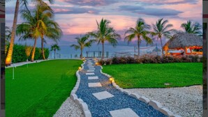 A pathway leading to a beach with palm trees and a thatched-roof structure. - Paradise Point -Pet friendly 
Oceanfront Luxury with Pool/ Dock/outdoor kitchen. (Marathon)