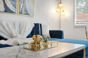 A modern living room with a marble coffee table, a blue sofa, abstract wall art, and a floor lamp.