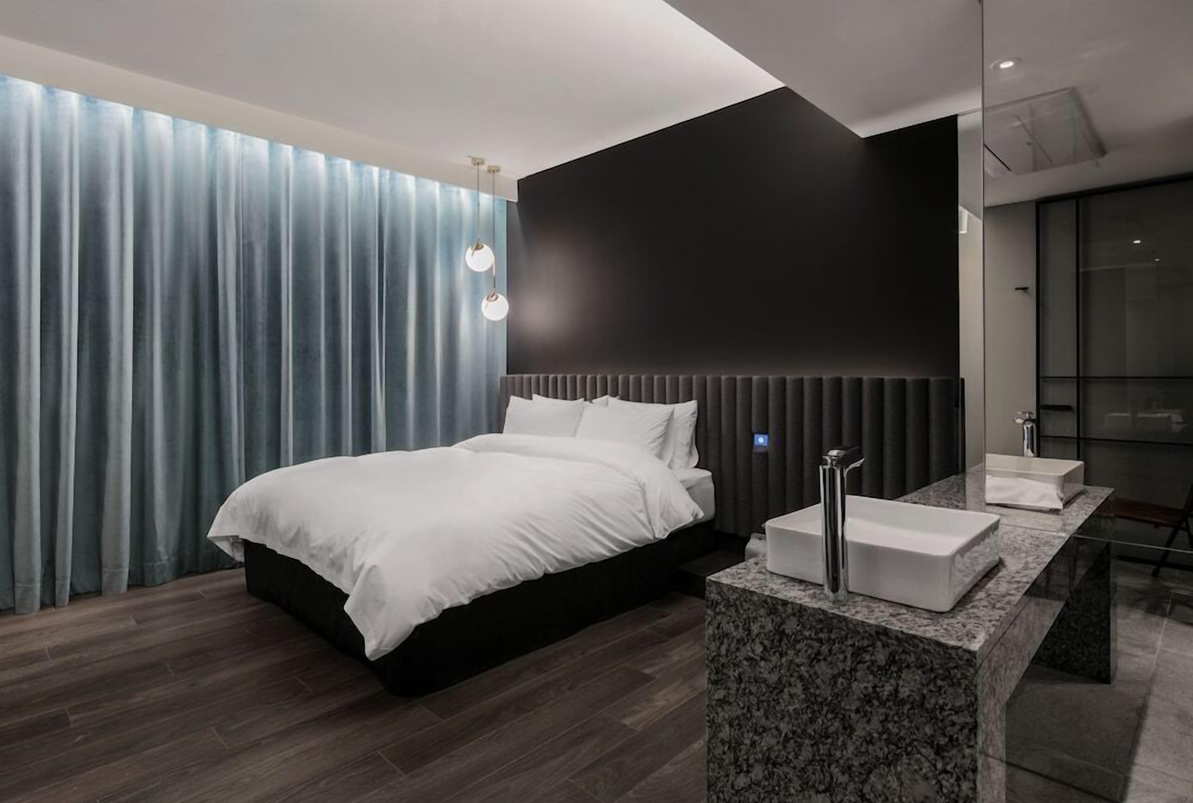 A modern bedroom with a bed, a marble vanity, and a dark accent wall.
