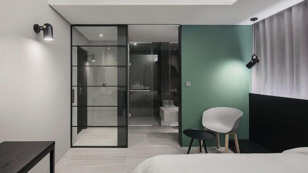 A modern hotel room with a bed, a chair, a desk, and a glass door leading to a bathroom. - H Hotel Wangsimni (Seoul)