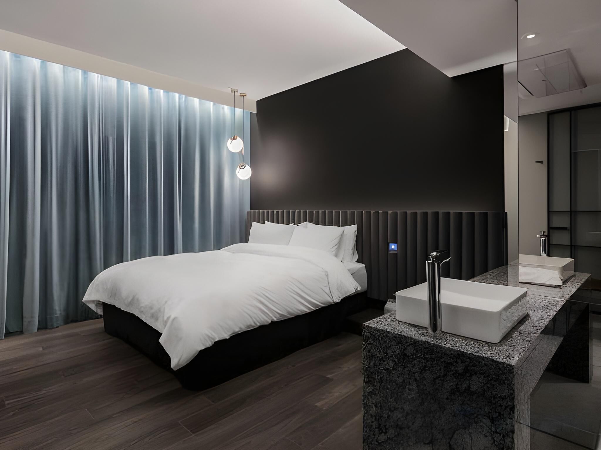 A modern bedroom with a large bed, a marble bathroom counter, and a dark accent wall.
