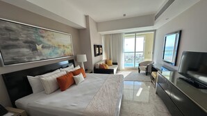 Habitación de hotel con una cama grande, televisor, escritorio y vistas al exterior.