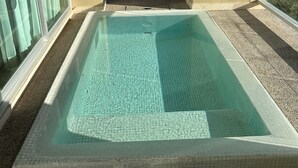 Una piscina con vistas despejadas al océano, un balcón con barandilla de vidrio y un edificio al fondo.