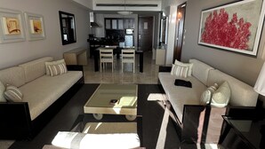 Una sala moderna con un sofá, una mesa de centro y una silla. Se ve un área de cocina al fondo con armarios y un refrigerador.
