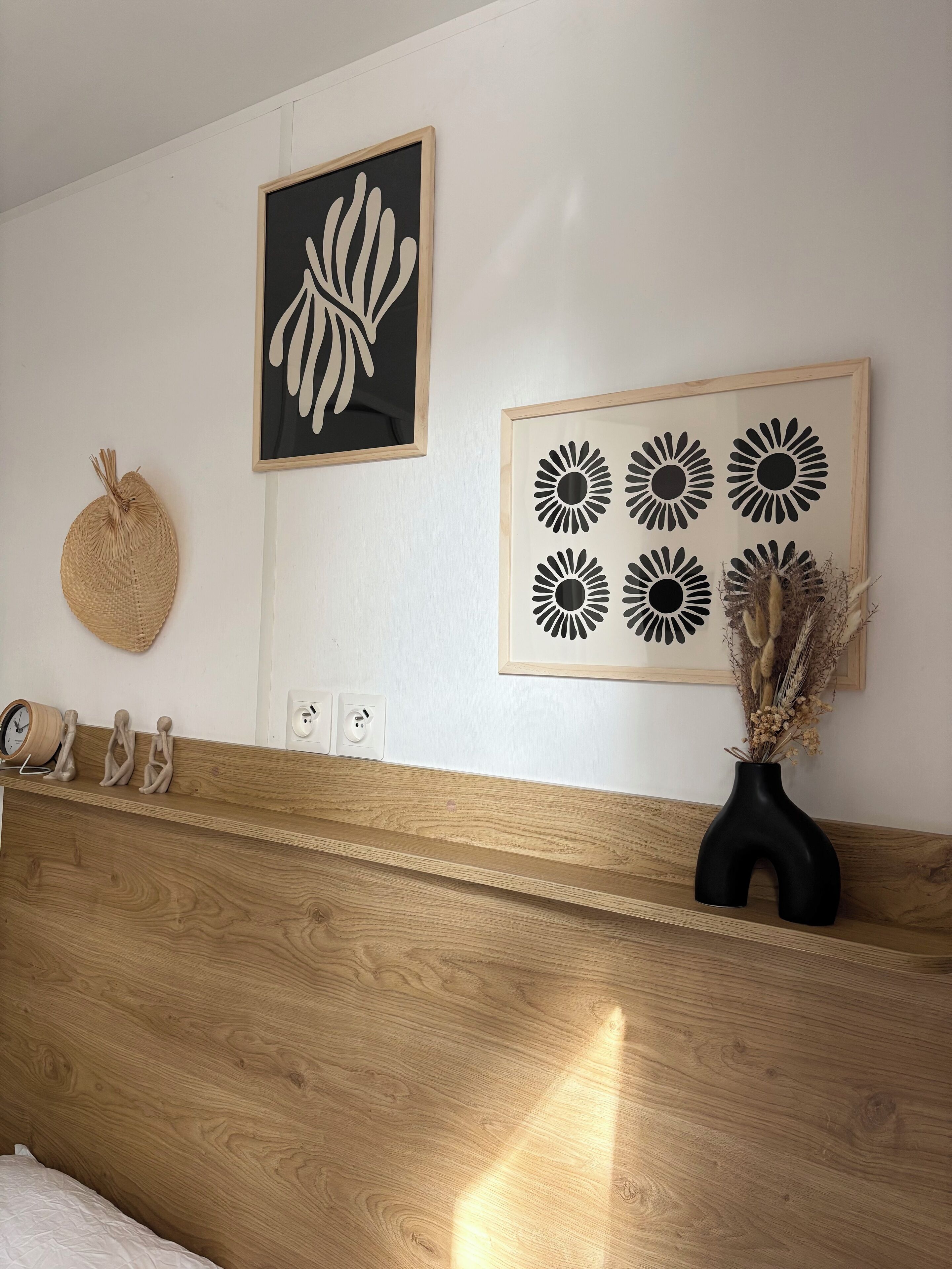 Ein Schlafzimmer mit einem Holz-Kopfteil, einer Uhr, Wandbildern und einer Vase mit getrockneten Blumen.