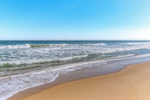 Ein Strand mit Wellen, blauem Himmel und sandigem Ufer.