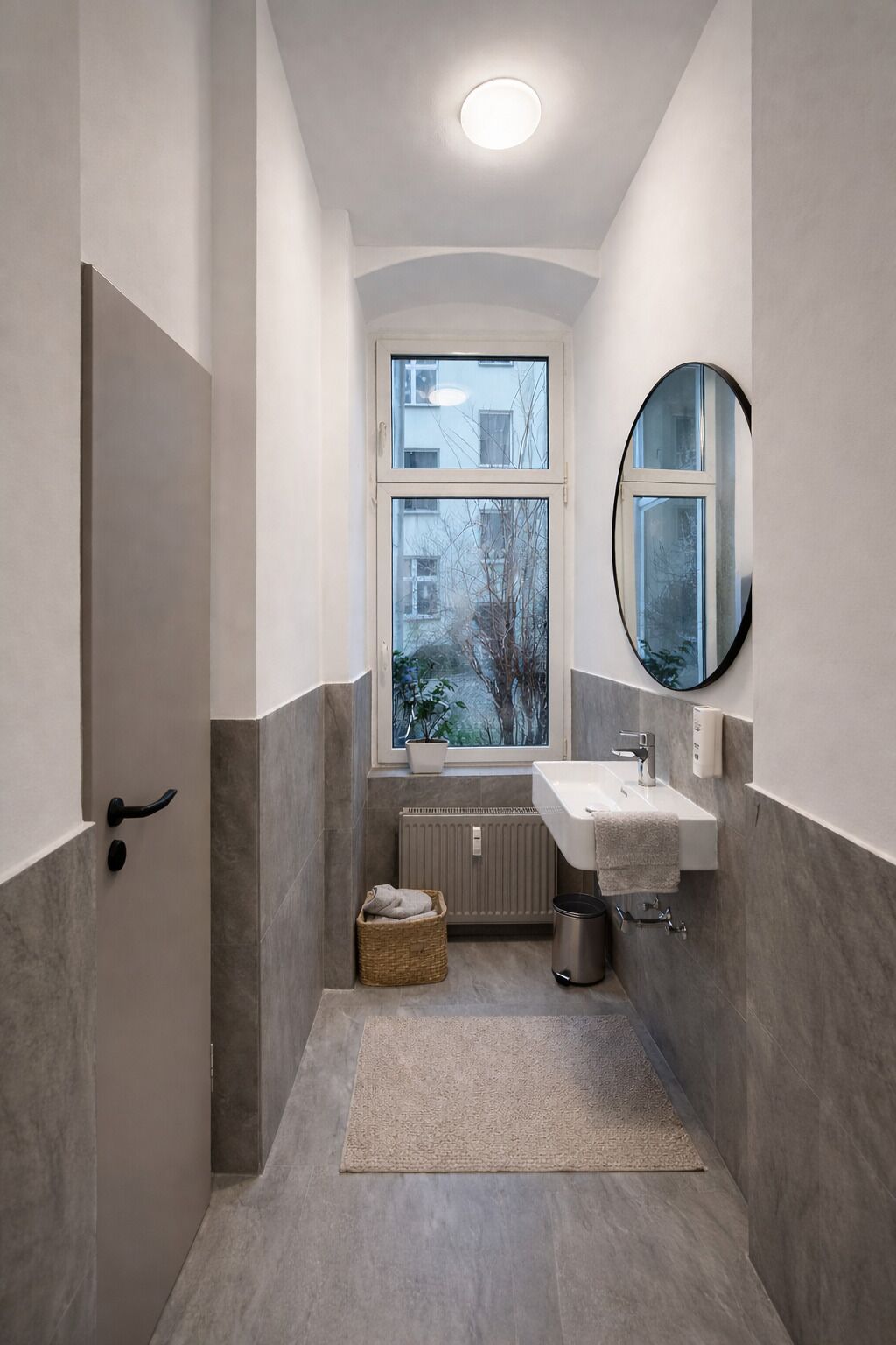 Un baño moderno con lavamanos integrado, un espejo redondo, una planta en maceta y vistas al exterior.