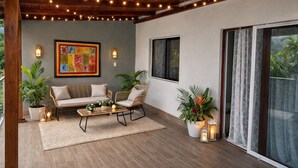 Un espace patio intérieur doté d’un plafond en bois, de guirlandes lumineuses, d’un tableau abstrait encadré, d’un canapé, de fauteuils, d’une table basse, de plantes en pot et d’une porte-fenêtre coulissante.