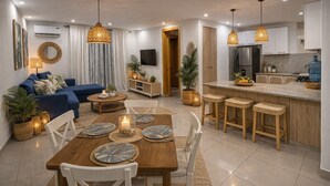 Une cuisine moderne dotée d’un îlot central, un coin repas avec une table et des chaises en bois, et un espace de vie agrémenté d’un canapé bleu et de plantes décoratives.