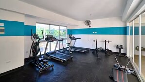 Une salle de sport équipée de tapis de course, d’un ventilateur et de matériel de musculation.